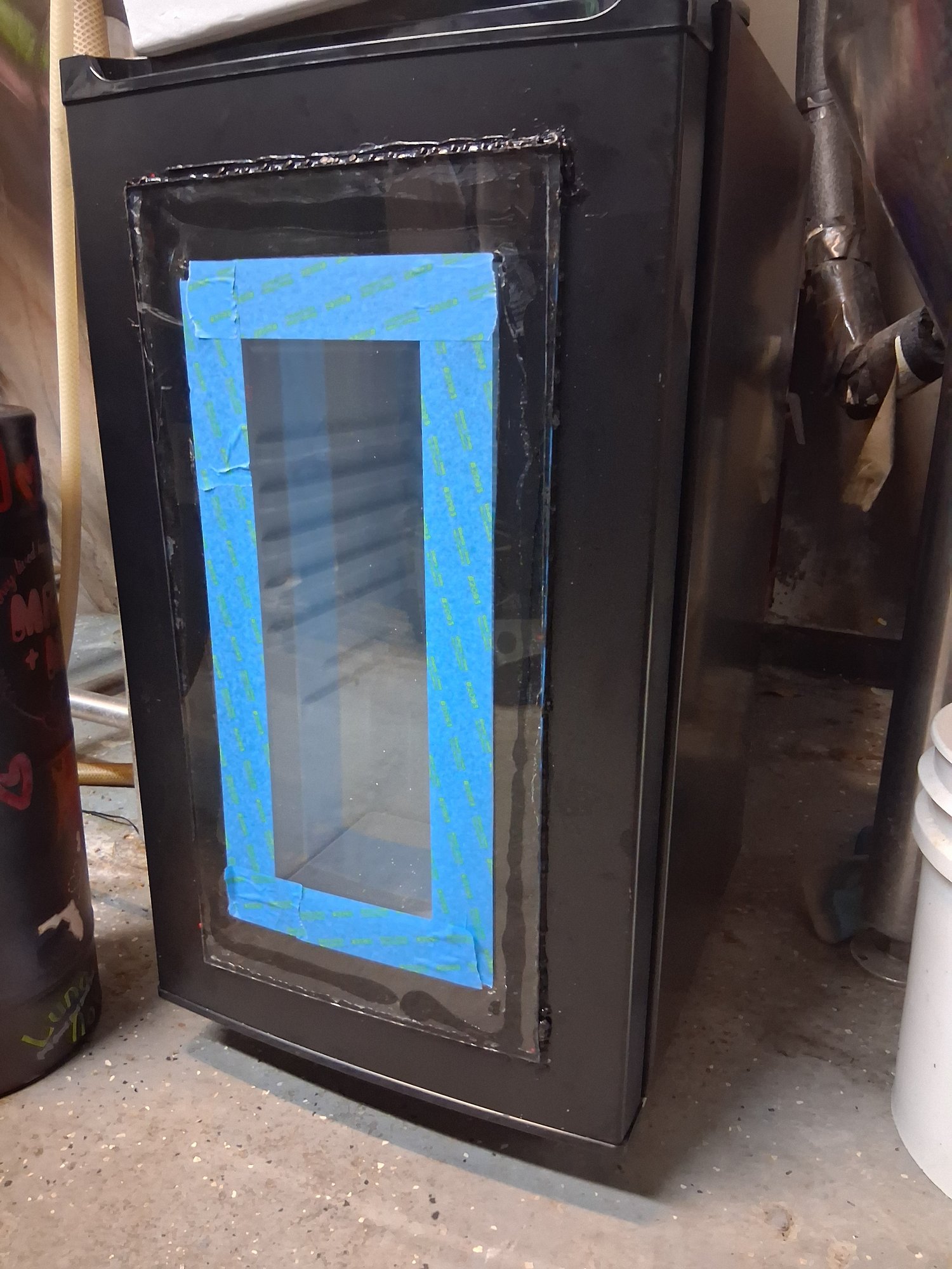 A black mini fridge with a taped-off glass window, being customized into a kegerator